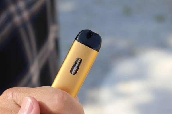 Close-up of a gold disposable vape held outdoors