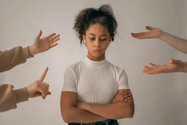 Girl with crossed arms surrounded by pointing hands, looking down