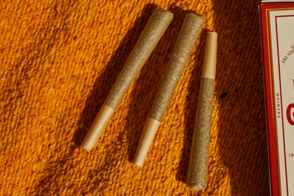 Three infused cannabis pre-rolls on an orange surface