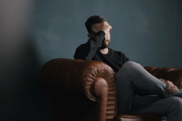 Man sitting on a leather couch with his hand on his forehead, showing the sluggish feeling of a cannabis hangover