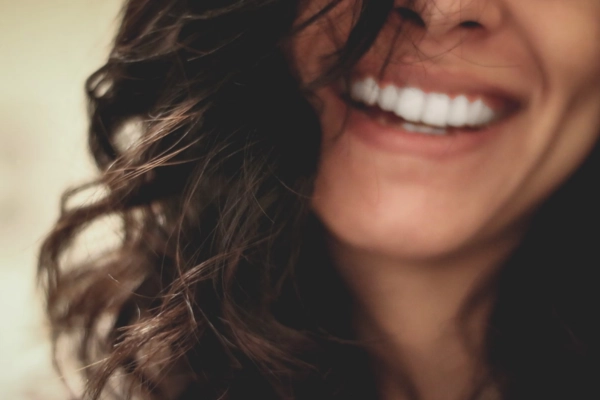 Close-up of a smiling person with curly hair, showing bright white teeth