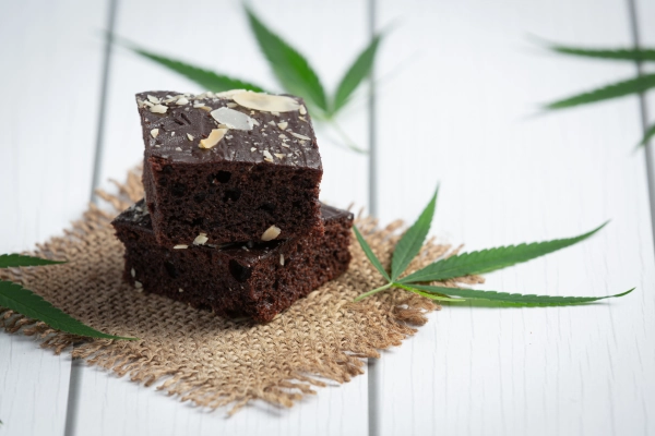 Two cannabis-infused brownies stacked on a rustic cloth with hemp leaves