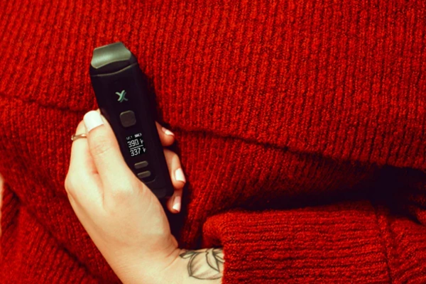 Person in a red sweater holding a black dry herb vaporizer set to 390°F, showing close-up of display and grip