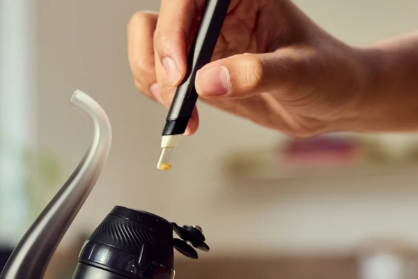 A person’s hand holding a dab tool with concentrate above a Puffco Proxy vaporizer