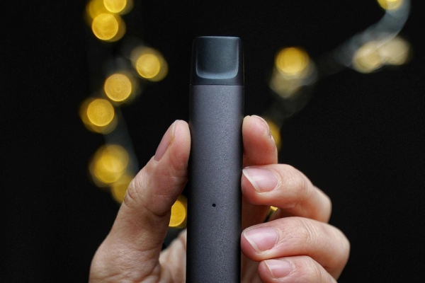 Hand holding a slim black disposable vape device against a dark background