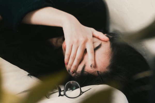 Person lying down with hand covering face, appearing mentally fatigued